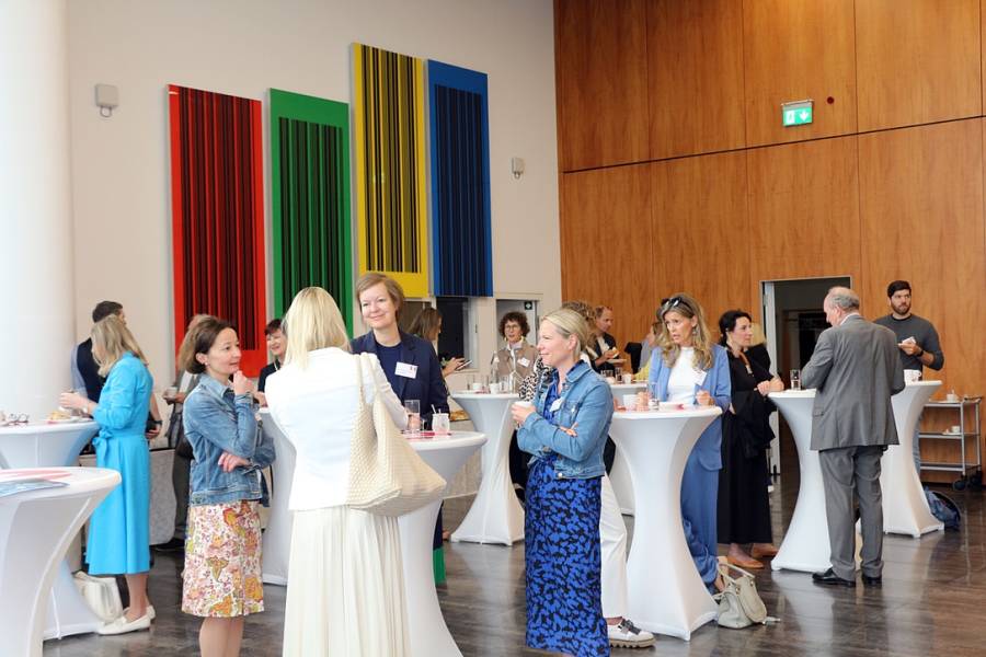 Menschen im Gespräch bei Stehtischen, bunte Kunstwerke an der Wand